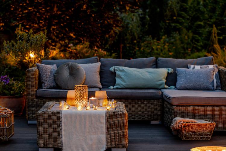 An outdoor decking area in the evening with a luxury rattan corner sofa, table and lit candles.