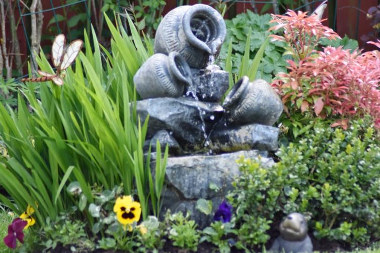 A water fountain amongst flowers and other garden ornaments. A water fountain is a top garden trend in 2021. 