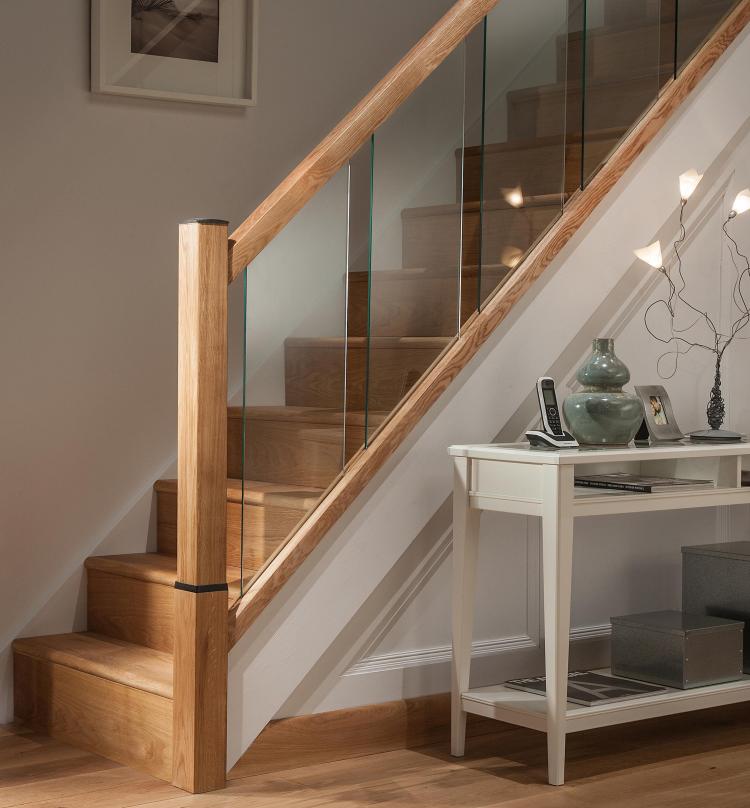 A picture of the Reflections Glass Balustrade range in a hallway including modern glass panels and oak handrails, base rails and newel posts.